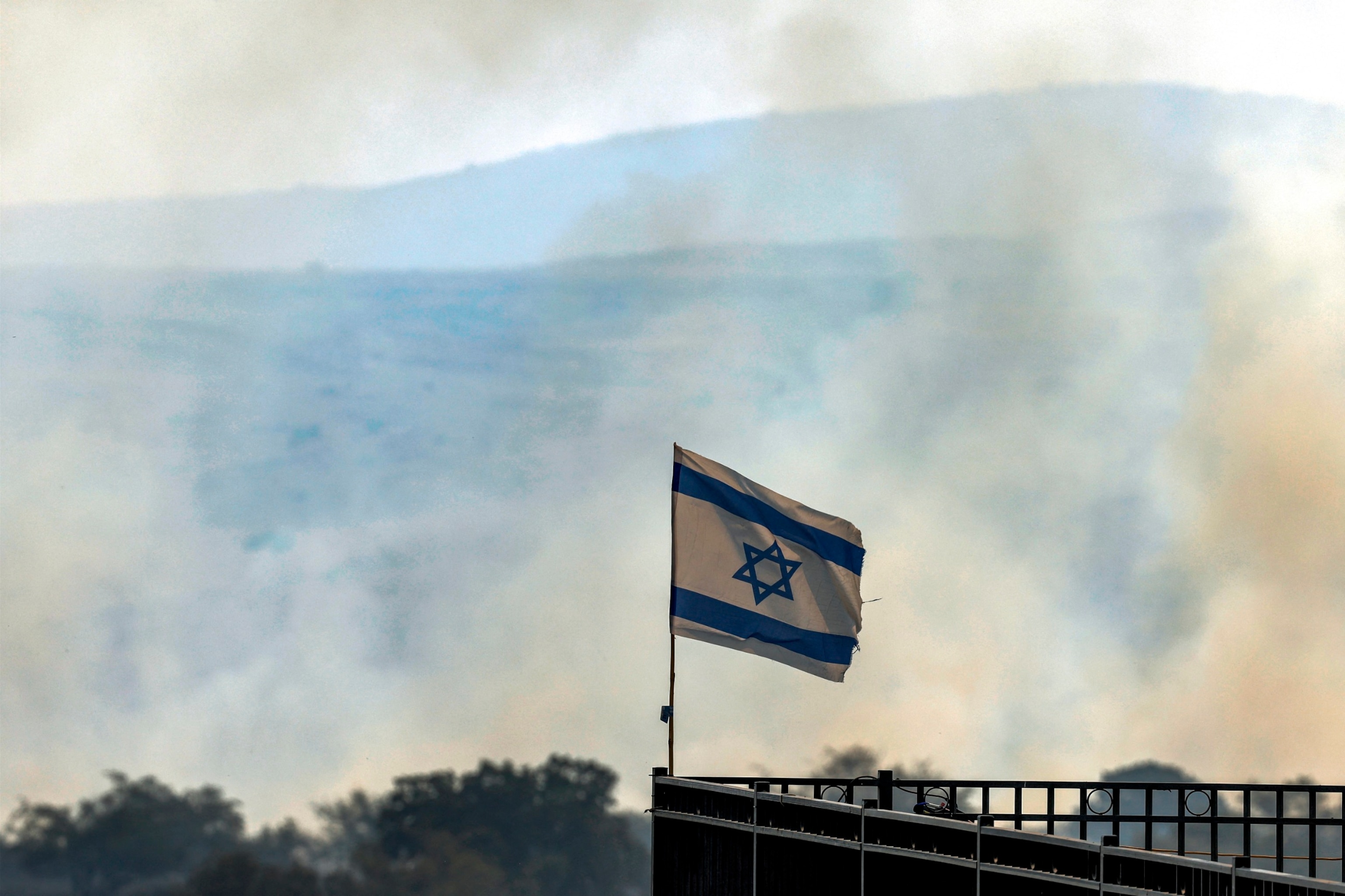 PHOTO: An Israeli flag flies from a pole as behind smoke plumes rise from a fire in a field after rockets launched from southern Lebanon landed near Katzrin in the Israel-annexed Golan Heights, June 13, 2024.
